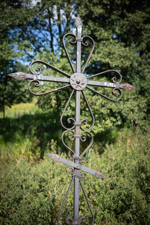 A metal cross is standing in the outdoor area. The cross is surrounded by leaves and has a metal stem.の写真素材