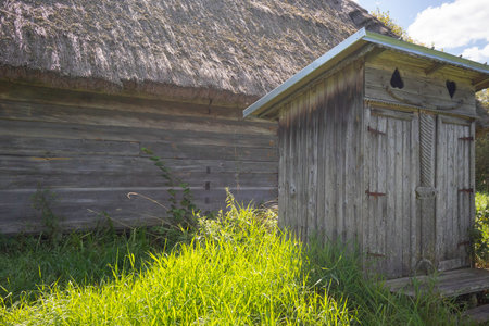 A small wooden building with a roof and a door. The building is surrounded by grassの写真素材