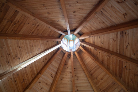 The wooden ceiling of a building has a circular hole in the middle. The wood is brown and the ceiling is open to the skyの写真素材