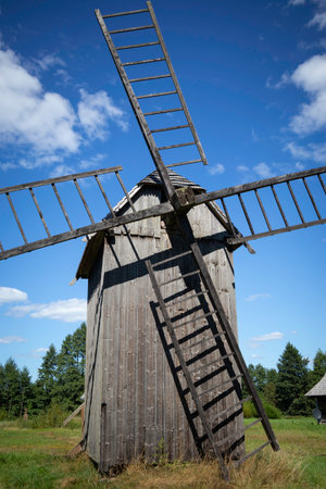 A windmill with wooden steps leading up to it. The windmill is old and has a rustic appearance. The sky is clear and blue, and there are trees in the backgroundの写真素材