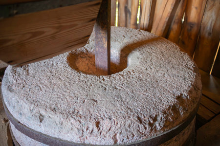 A large, old-fashioned stone grinding wheel with a wooden handle sits in a rustic setting. The wheel is made of stone and has a wooden handle, which is used to turn the wheelの写真素材