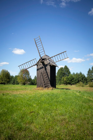A windmill is standing in a field of grass. The sky is clear and blue. The windmill is old and has a ladder leading up to itの写真素材