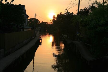 Silhouette scene  light reflection on the canal at rural village before sunsetの写真素材