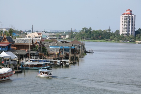 Thai wooden ferry heading to the dock near traditional riverbank village の写真素材