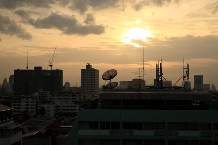 Sihouette satellite dish and 3G antenna on top of building against sunsetの写真素材