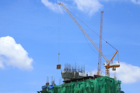 Yellow tower crane on top of building against blue sky の写真素材