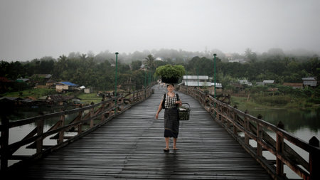 SANGKLABURI-AUG 14  An unidentified Mon woman carrying vegetable basket on head at wooden bridge in Sangklaburi, Thailand on August 14, 2011  Carrying things on the head is Mon traditional culture  のeditorial素材