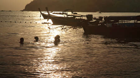 Silhouette scene of rim light on Andaman sea while people swimming near the boatsの写真素材