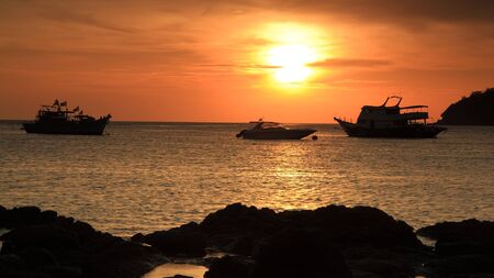 Tropical sunset scene while ferry and boats floating on Andaman sea at Koh Lipe island in Thailandの写真素材