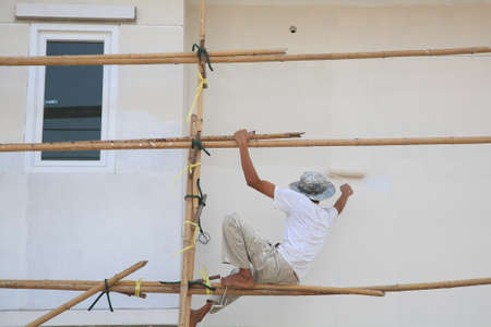 Worker on wooden scaffold painting wall of construction building の写真素材