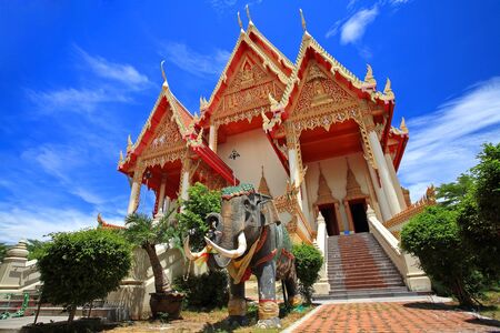 Elephant statue in front of large temple  against blue sky at Wat Ketumwadee Sri Wararam in Samut Sakhon, Thailandの写真素材