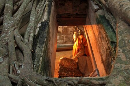 Buddha statue view from a window with Bodhi tree root covering ancient temple of Wat Bang Kung at Amphawa in Samut Songkhram, Thailand の写真素材
