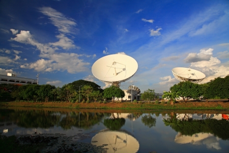 Large broadcast radars or satellites with reflection on the pond against blue skyの写真素材