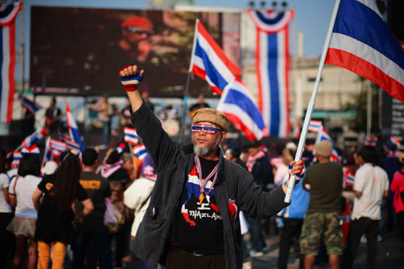 BANGKOK - JAN 25: Unidentified old protester with dress decorations raises Thai flag to anti government at Ladprao street on January 25, 2014 in Bangkok Thailand.のeditorial素材