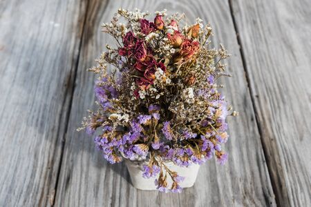 Purple flower and dry rose in pot on wooden tableの写真素材