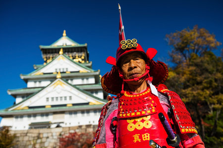 OSAKA, JAPAN - NOVEMBER 26, 2016: Unidentified Japanese old man with red samurai suit at Osaka castle with blue sky. Here is the most famous Osaka visitor landmark.のeditorial素材