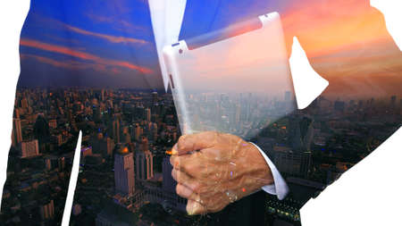Business man holding tablet overlay of aerial skyline cityscape at twilightの写真素材