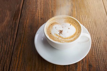 Hot cappuccino coffee with smoke in white cup on wooden tableの写真素材