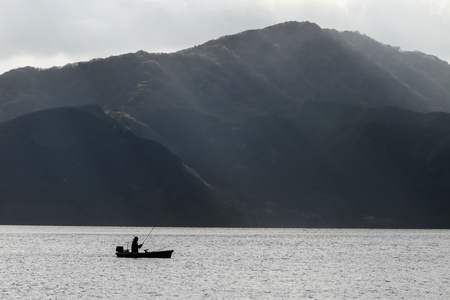 Fishing on Ashi lake with sun rays against the mountain, Hakone, Japan. Black and white processの写真素材