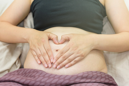 Pregnant woman making hands sign of heart shape on belly. 26 weeks old babyの写真素材
