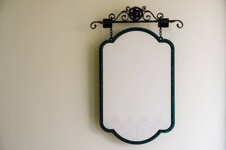 Blank hanging white iron plate sign with floral pattern  attached on white wallの写真素材