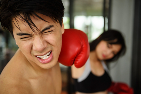 Asian handsome man face punched by beautiful girl right hand with red boxing glove. Fitness and gym for healthy concept.の写真素材