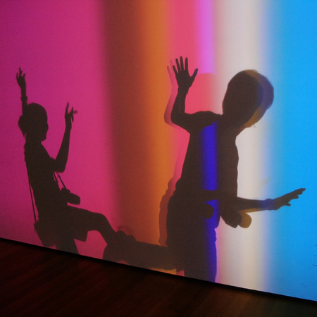 Silhouette shadow of two happy young couple create fun body posting of white wall with colorful light spotsの写真素材