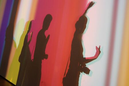 Silhouette shadow of three happy people make Buddhist hand sign posting on white wall with colorful light spotsの写真素材