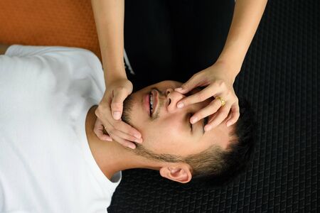 Closeup of unconscious Asian male and female hands holding his nose and opening mouth to save his life after heart attack in fitness floor. Safety and Healthcare conceptの写真素材