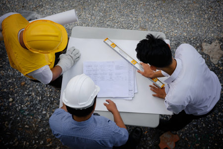 Engineering team of site manager, young engineer, and foreman looking paper plans at construction...
