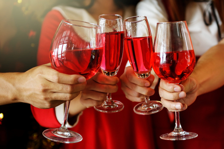 Group of young hands with red wine toasting glasses for Christmas or xmas celebrating party. Closeup photo with bokeh background for ceremony holiday celebration.の写真素材