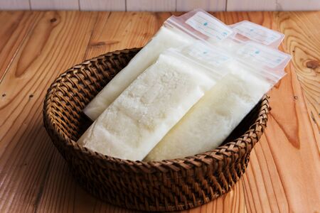 breast milk frozen in plastic storage bags on rattan wicker basket on brown wooden table for newborn baby.の写真素材