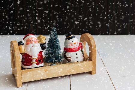 Santa claus, xmas tree, snowman on wooden container above white wooden table with motion heavy snowfall and copy space for text. Christmas and New year celebration concept for interior decoration and advertisement.の写真素材