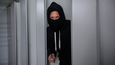 Asian murderer or thief man in black hoodie jacket and mask holding a knife and waiting for a female victim in woman toilet or restroom. criminal and robbery for public safety concept.の写真素材