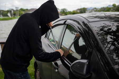 Robber man in black hoodie jacket and mask using a crowbar on his hand to break lock and steal a vehicle. Car thief or theft for insurance conceptの写真素材