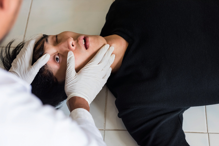 Doctor or detective checking left eye during  performing autopsy or postmortem of death young man by overdose. Drug addiction and social issue for teenager, student, and worker.の写真素材