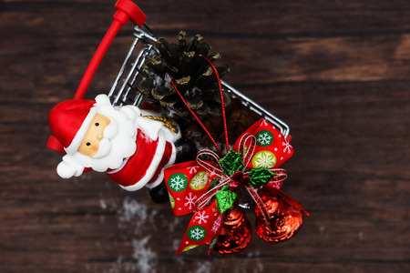 Top view of X'Mas red santa claus, bell, Pine cones on red small shopping cart with old wood table and copy space for text, Thanks giving day and  christmas decoration objects arrangement.の写真素材