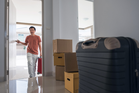Happy handsome husband man open front door of new house with many moving boxes and luggage inside blank home. Family lifestyle to start new life with modern interior.の写真素材