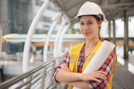 Portrait of Beautiful American young woman engineer with white helmet hat and engineer paper blueprint work at modern city. Construction project in urban town. International joint venture industry.の写真素材