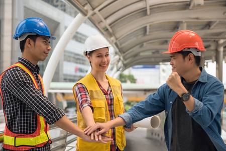 Engineer team of Asian men and American woman stacking hands to encourage each other. International joint venture to work construction building project in city. Teamworkの写真素材