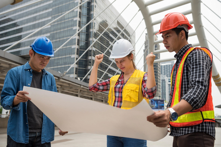 Angry and stress American woman boss look at blueprint paper plan and blame Asian engineering men team for project delay. International joint venture to work construction building in city.の写真素材