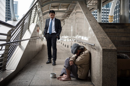 Kind Business man with black suit look at sad beggar man or old homeless guy at city walk in urban town. Poverty and social issue concept. Give and share with sympathy.のeditorial素材