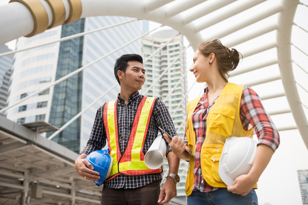 Happy Engineer team of Handsome Asian man and beauty American woman look at each other to encourage . International joint venture to work construction building project in city. Success Teamworkの写真素材