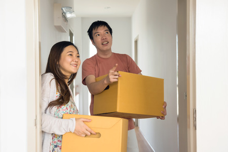 Happy young Asian couple carry cardboard boxes to move stuffs to master bedroom of new house. Smile Wife and Husband moving to new empty home to start new life. Architecture and Real estate industry.の写真素材