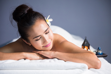 portrait of young happy Asian beautiful woman relax in spa. Body care treatment. Cute girl having massage at back by professional massager hands with candle and white Plumeria on bed.の写真素材