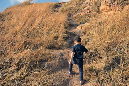 Healthy young boy clinbing  and hikking to top of moutain by flipflop. Walking at danger steep hill slope with natural meadow background.の写真素材