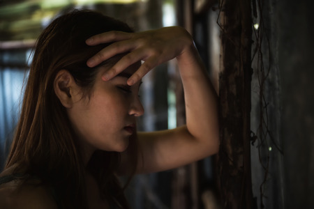 Stressed Asian beautiful woman get headache in abandoned house. Depress girl hand touching head at grunge wood and wall.の写真素材
