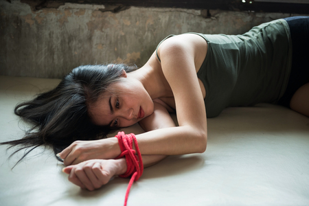 Sad female bvctim hands tied by red rope in abandon house. Hostage concept or female kidnapped from robber. Sexual abuse or rape in dirty room with copy space for text.の写真素材