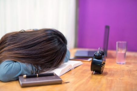 Tired student woman in house sleep on text book above working table. Serious exhauasted Asian girl wok hard by reading book to prepare for final exam.の写真素材