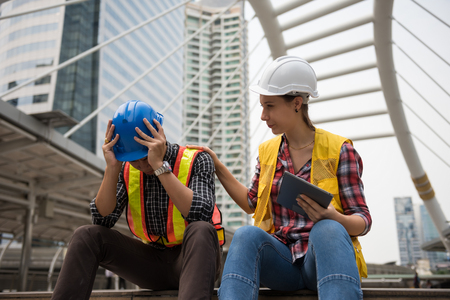 Sad engineer raise hands to relief headache while American female manager try to cheer him up. Depress or stressed working man after construction project fail. Fired or sack from job.の写真素材